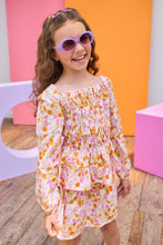 Load image into Gallery viewer, Young girl wearing a floral top and skirt with sunglasses in front of colorful geometric shapes.