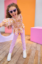 Load image into Gallery viewer, Child wearing a floral top and purple pants with colorful background