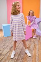 Load image into Gallery viewer, Two young girls in purple dresses standing in a room with a wooden floor and colorful walls.
