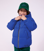 Load image into Gallery viewer, A smiling child wearing a bright royal blue puffer jacket,
