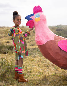 Child holding a large inflatable pink rooster in an open field